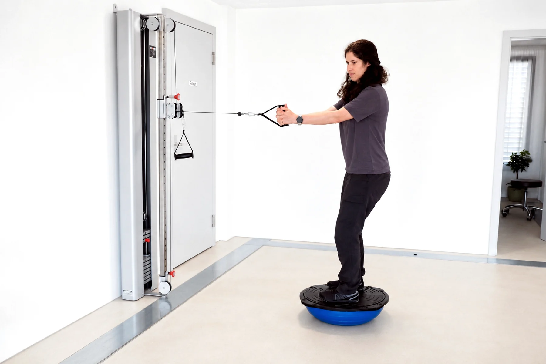 MEDOS-Therapeutin demonstriert eine Gleichgewichtsübung am Seilzug auf einem Balanceboard.