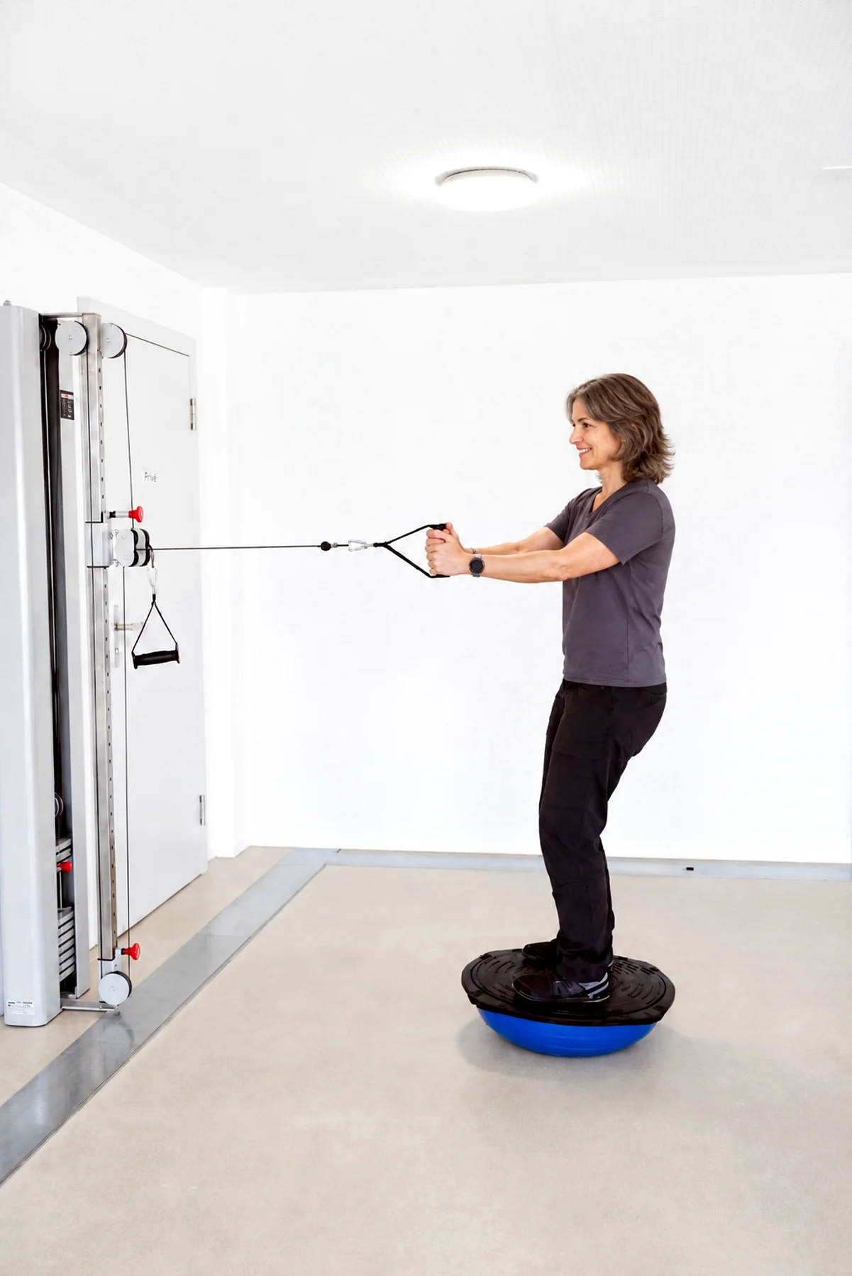 Therapeutin bei einer Gleichgewichtsübung mit Balanceboard und Seilzug